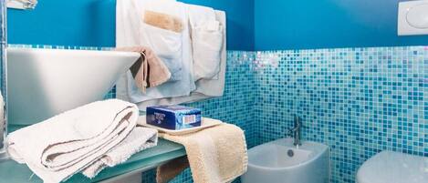 Een badkamer met een blauwe betegelde muur, een rond raam, een wastafel, een toilet en een klein mandje.