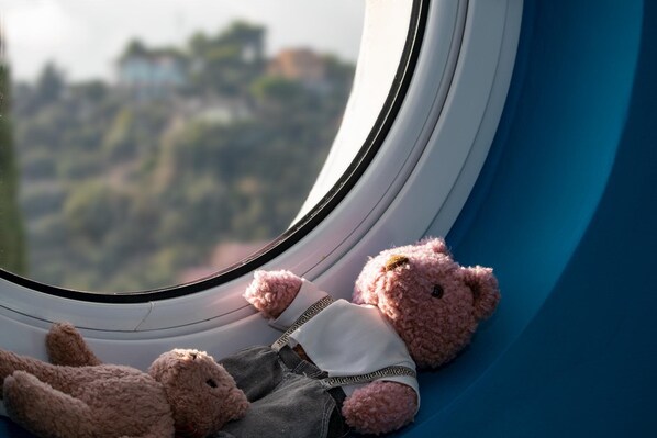 Un oso de peluche sentado junto a una ventana con vistas a un paisaje urbano.