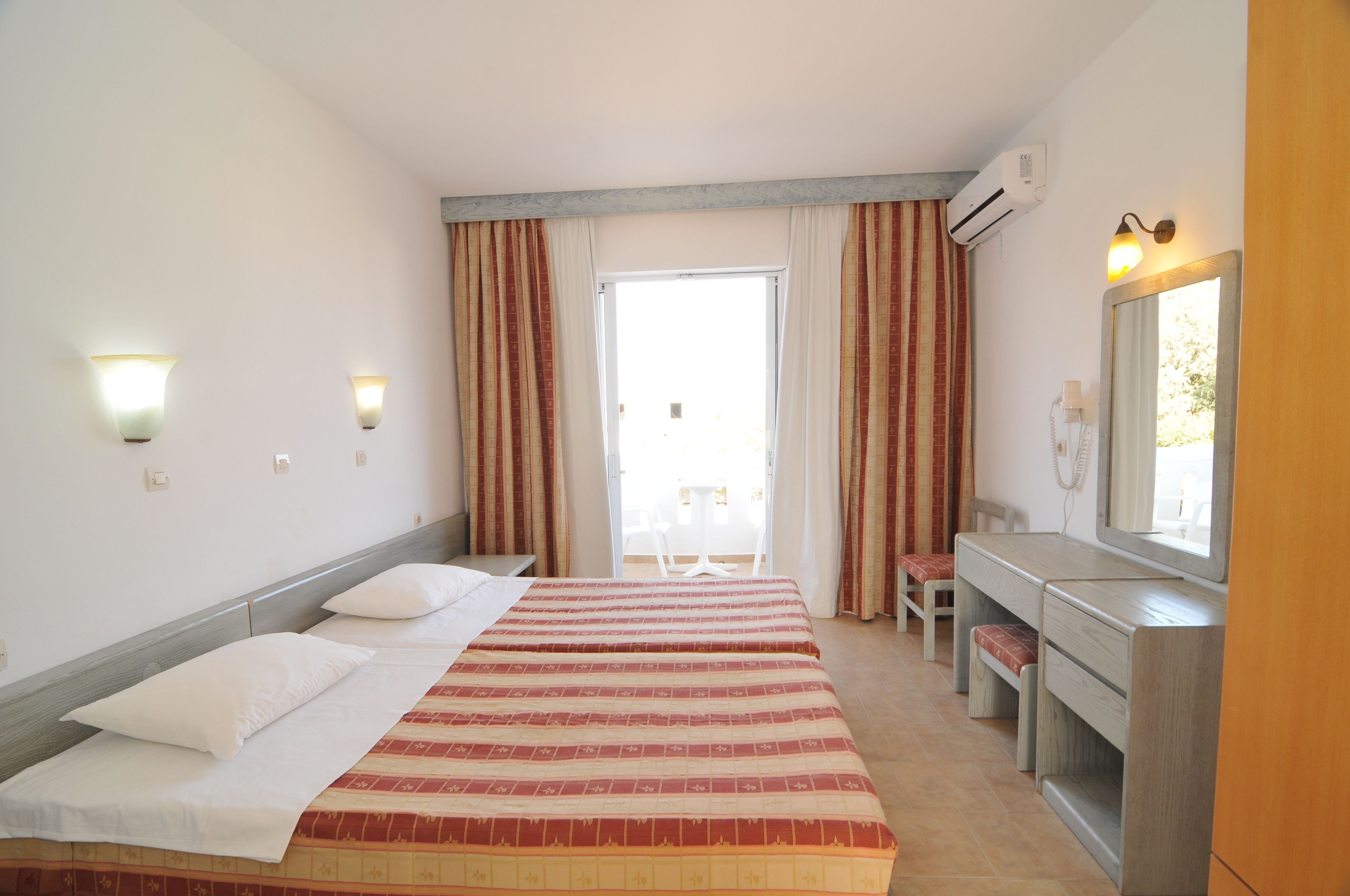 A hotel room with a bed, a desk, a chair, a mirror, and a window with curtains.