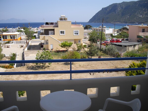 A balcony with a table and chairs, overlooking a residential area with houses, a parking lot, and a view of the sea and mountains. - Fourtounis Hotel (Kos)