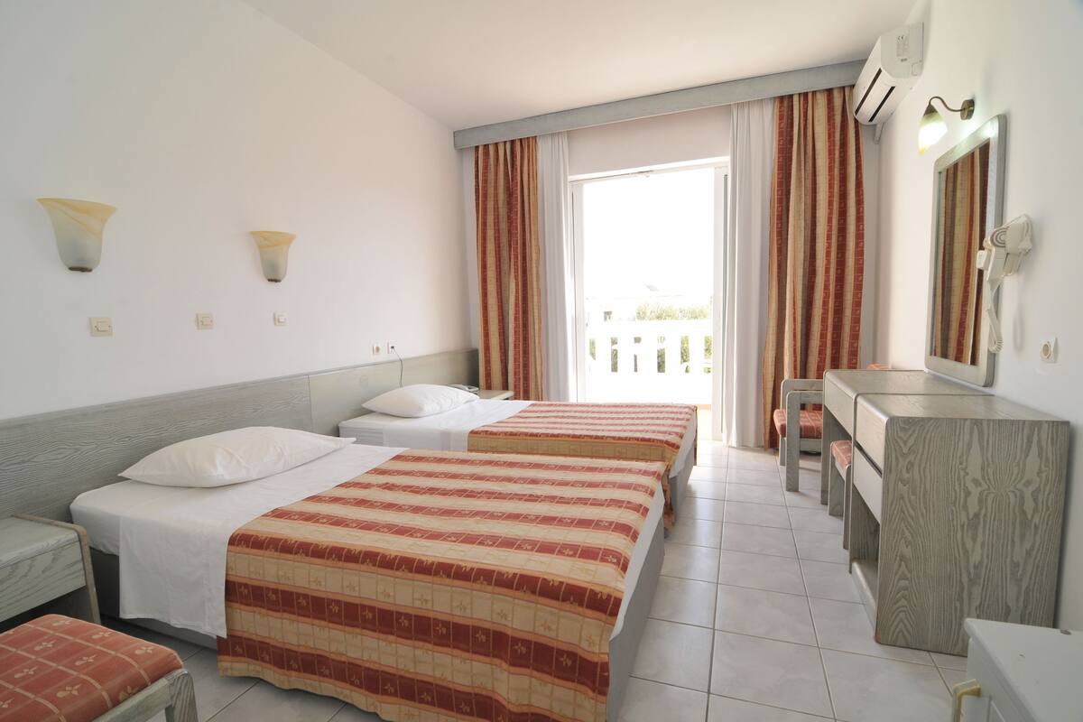 A hotel room with two beds, a desk, a mirror, and a window with curtains.