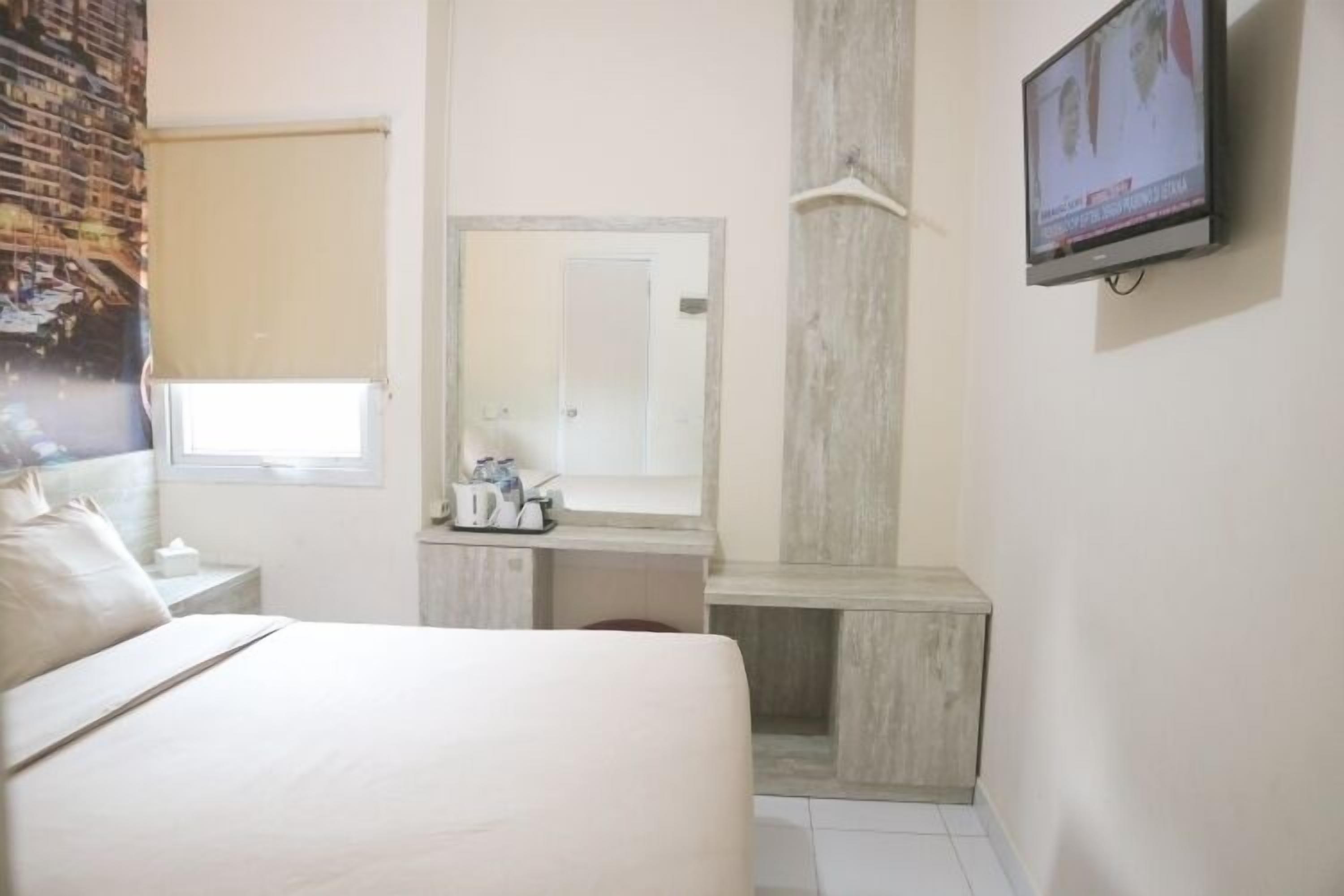 A hotel room with a bed, a large mirror, a television, and a small table with toiletries.