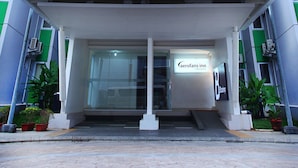 Entrada moderna de hotel com fachada de vidro, uma placa com o texto "Aerofans Inn" e uma galeria coberta.