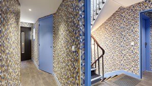 A hallway with patterned walls, a blue door, and a staircase with a handrail. - Hôtel Miramar (Paris)