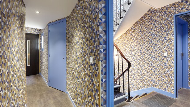 A hallway with patterned walls, a blue door, and a staircase with a handrail. - Hôtel Miramar (Paris)