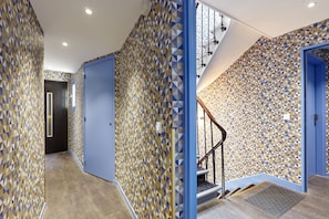 Un couloir aux murs ornés de motifs, une porte bleue et un escalier muni d’une main courante.