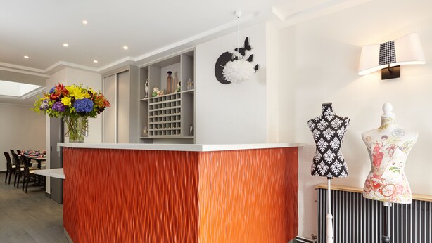 A reception area with a wooden reception desk, a wall-mounted lamp, and a mannequin. - Hôtel Miramar (Paris)
