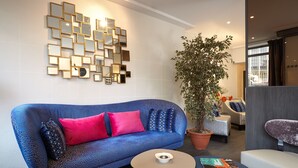 A modern living room with a blue sofa, a coffee table, and a wall of mirrors. - Hôtel Miramar (Paris)