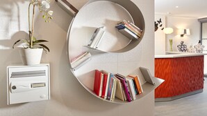 A modern reception desk with a circular mirror, a potted orchid, and a bookshelf with books and a laptop. - Hôtel Miramar (Paris)
