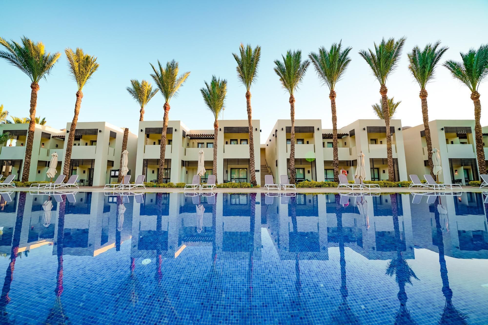 Un hotel con piscina, palmeras y arquitectura moderna.