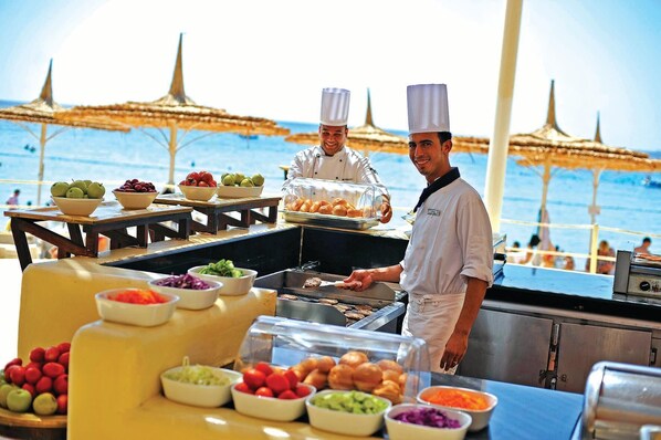 A chef preparing food at a seaside buffet with various fruits and vegetables displayed. - SENTIDO Reef Oasis Aqua Park Resort - All inclusive (Sharm El Sheikh)