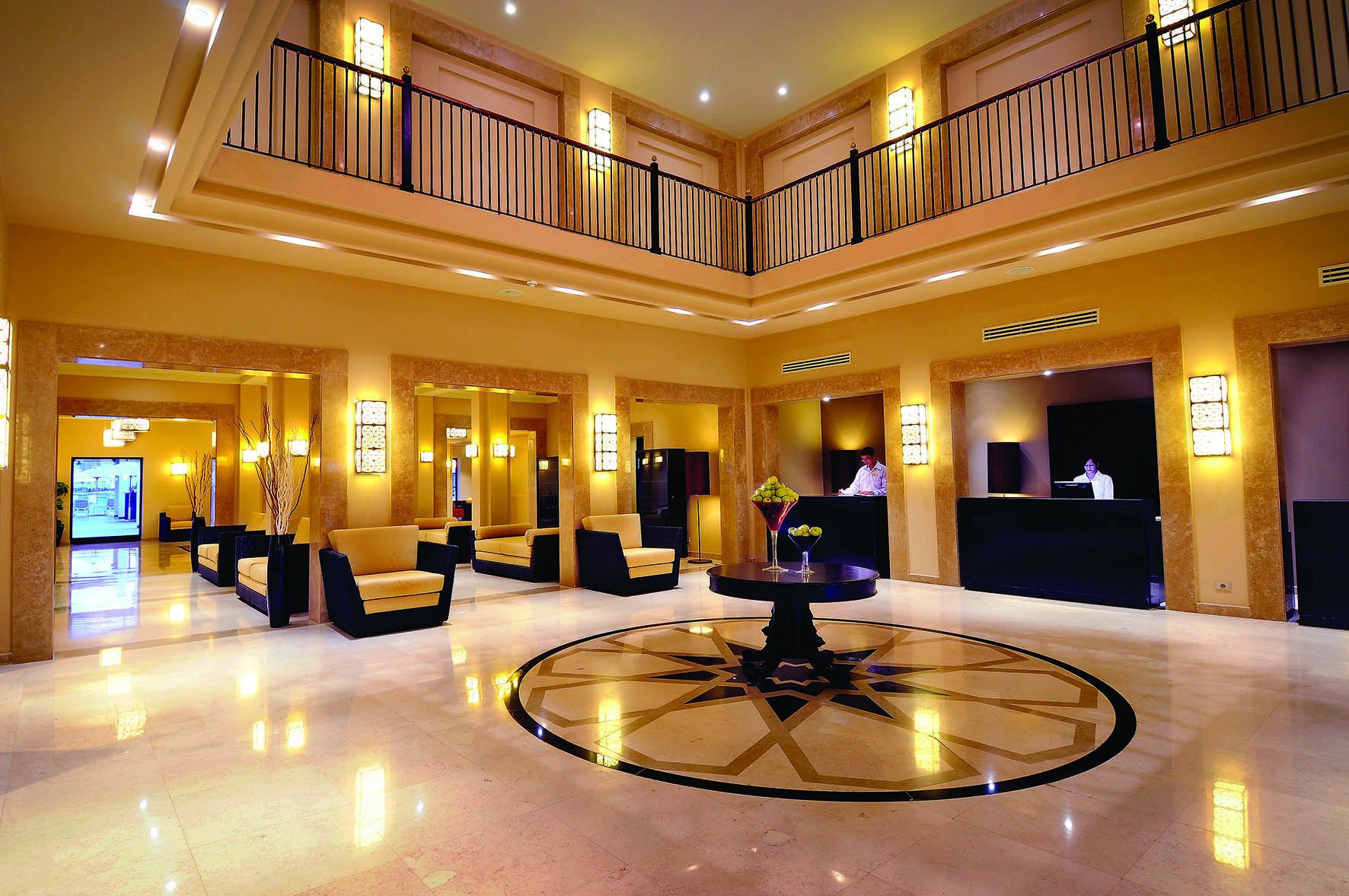 A spacious lobby with a central round table, multiple seating areas, and a reception desk.