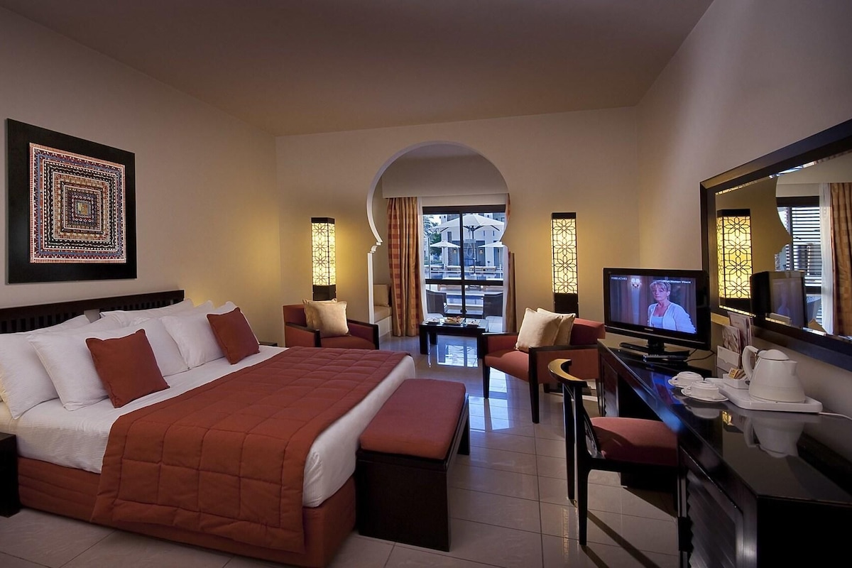 A hotel room with a large bed, a desk with a television, and a view of the outside.