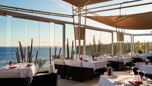 A restaurant with tables set for dining, large windows offering a view of the sea, and a ceiling fan. - SENTIDO Reef Oasis Aqua Park Resort - All inclusive (Sharm El Sheikh)