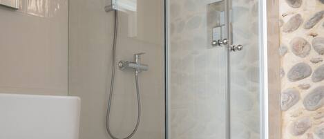 A modern bathroom with a glass-enclosed shower, a white sink, and a stone wall.