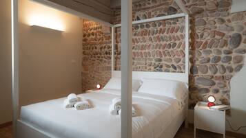 Een slaapkamer met een stenen muur, een bed met witte lakens en twee nachtkastjes met rode lampen.