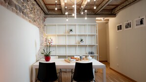 Comedor con mesa blanca, sillas negras, pared de piedra y techo de madera.
