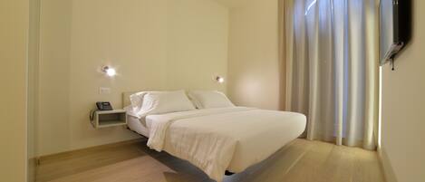Un dormitorio con cama, mesita de noche y televisor montado.