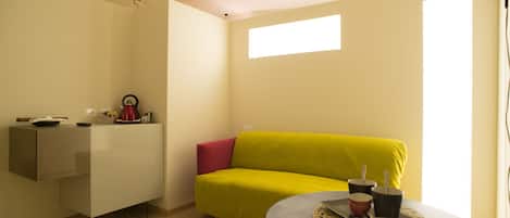 A small, bright room with a yellow sofa, a small table with cups and a plate, and a white cabinet.