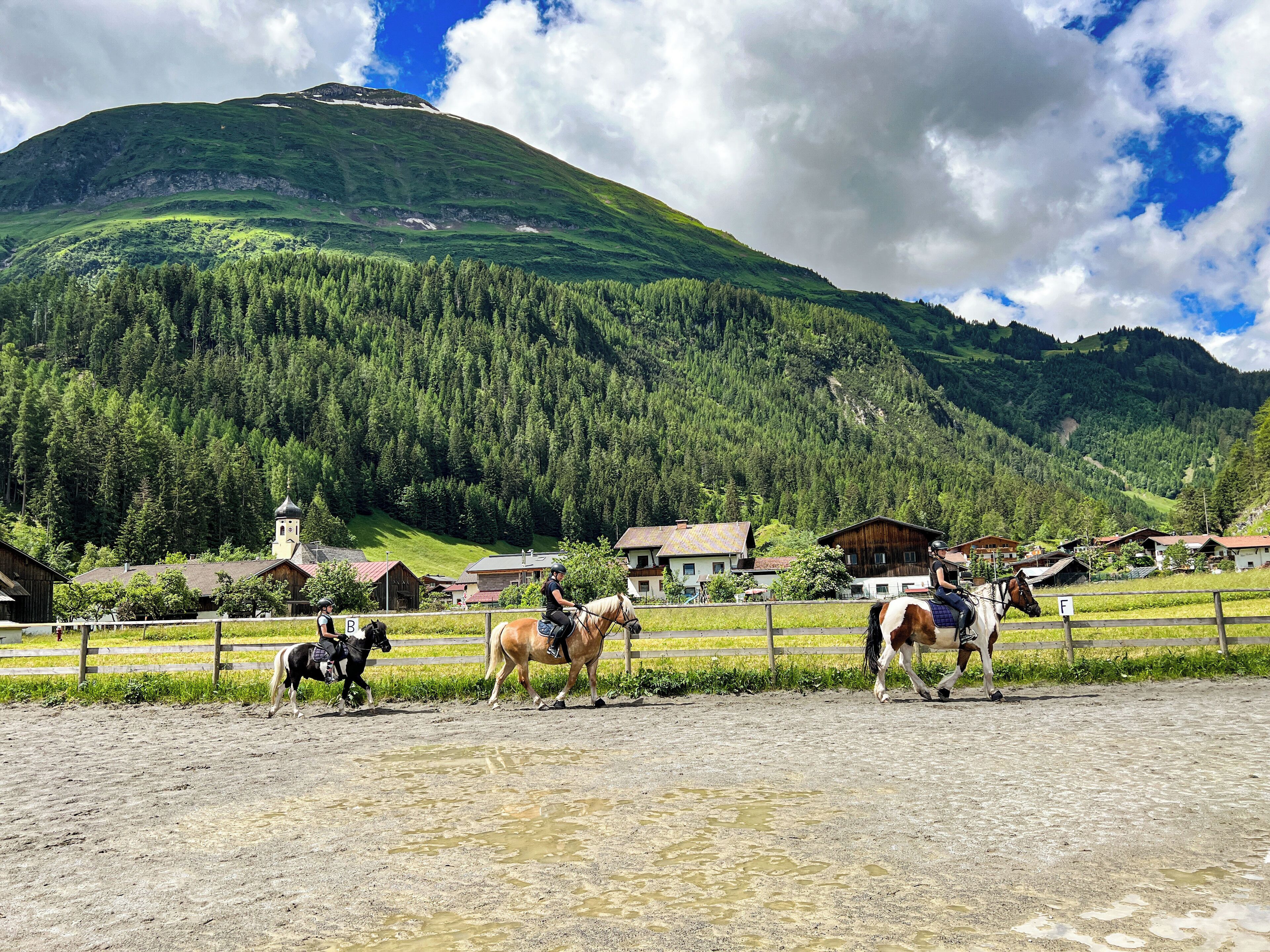 A rural setting with a mountain in the background, a fenced riding area, and a few buildings.