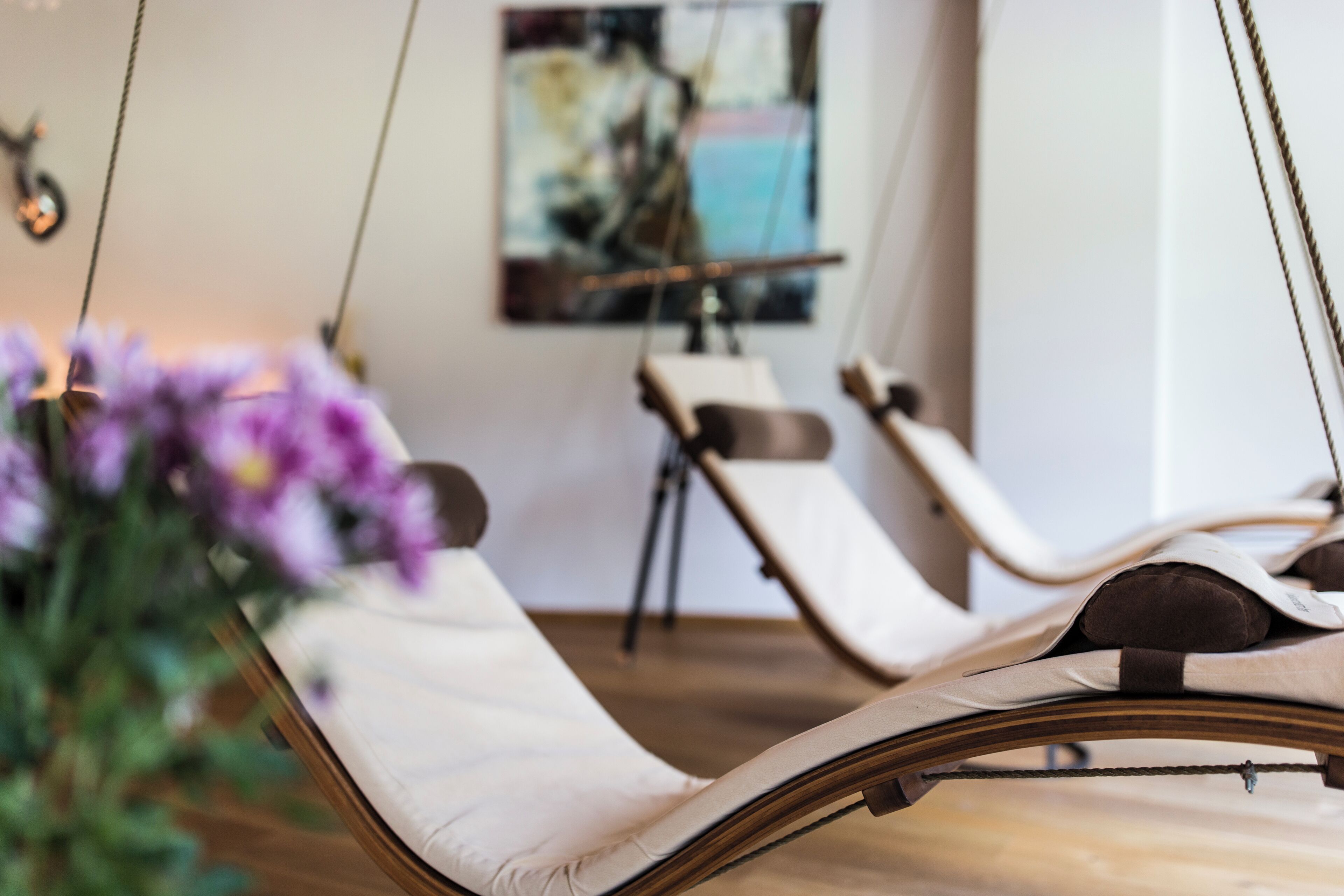 A room with a hanging chair, a painting on the wall, and a potted plant.