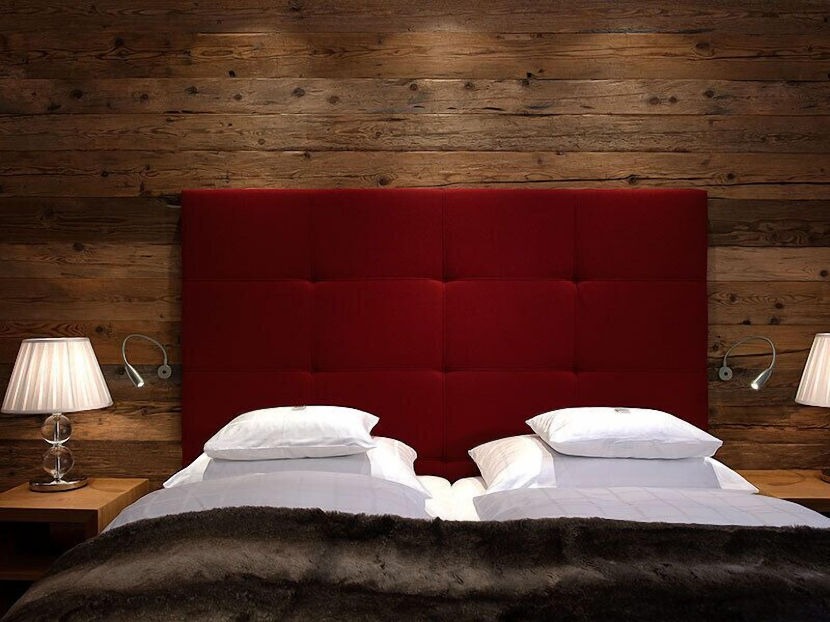 A bed with a red upholstered headboard, white pillows, and a dark fur throw.