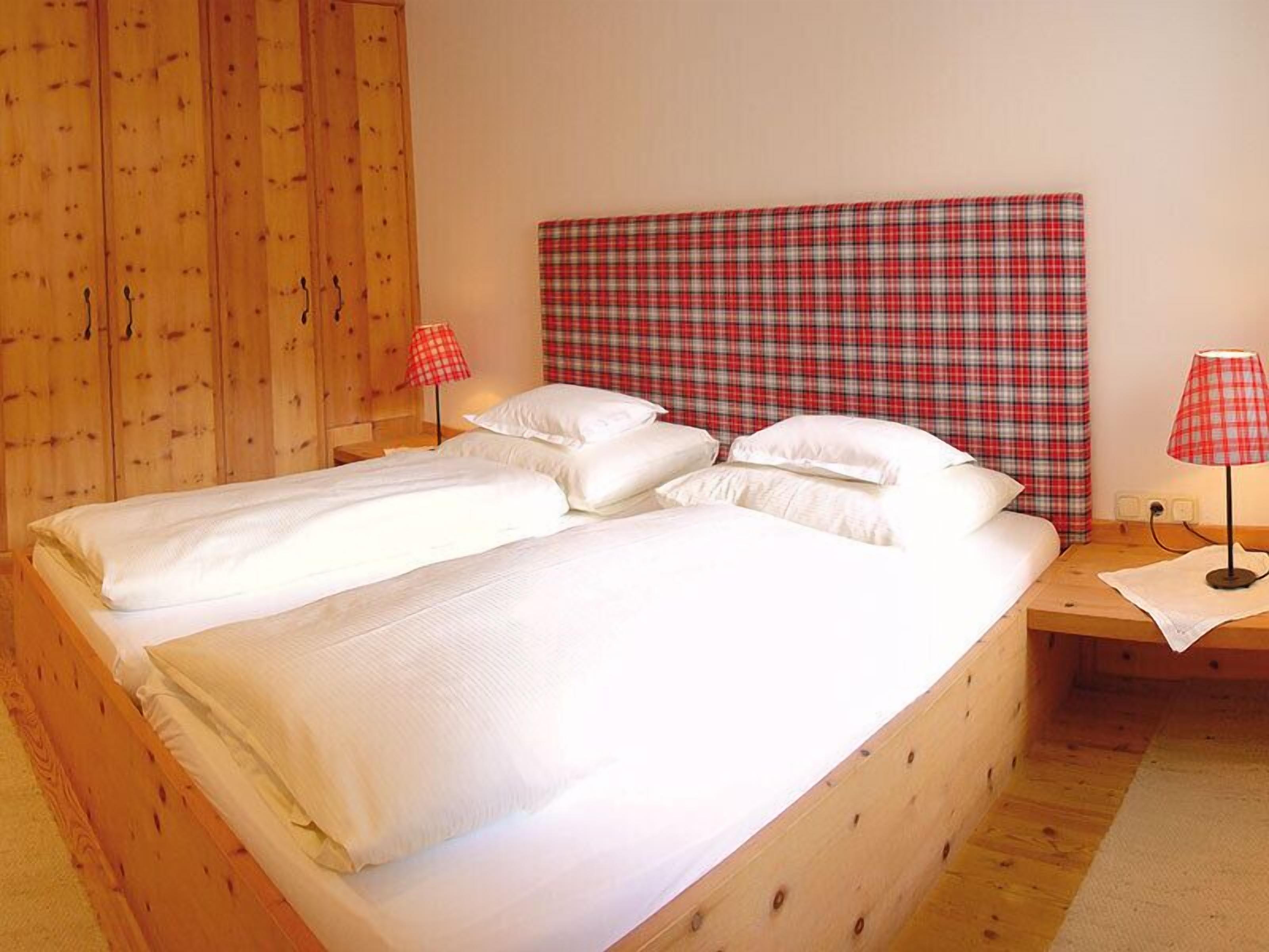 A double bed with white linens in a room with wooden walls and a plaid headboard.