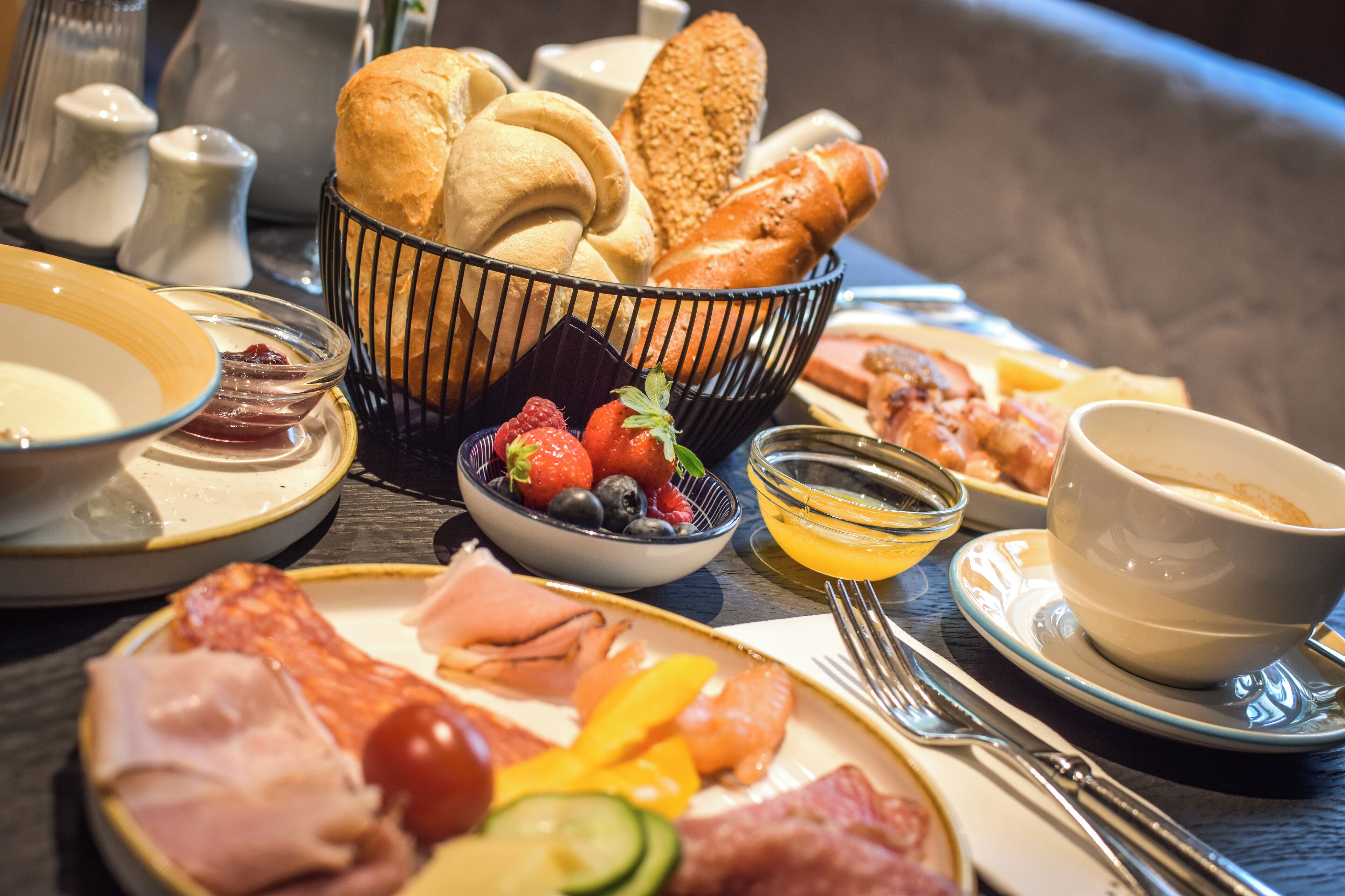 Un bufé de desayuno con panes, frutas y embutidos variados.