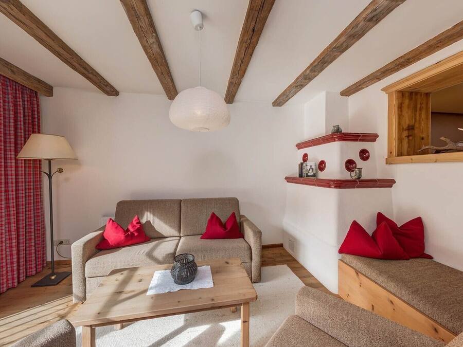 Un salon chaleureux avec un canapé, une table basse et un banc en bois. On y trouve une fenêtre avec des rideaux, une lampe et une étagère ornée d’objets décoratifs.