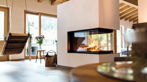 A modern living room with a fireplace, wooden flooring, a hanging chair, and large windows.