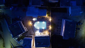 Vue aérienne d’un quartier résidentiel avec une piscine, plusieurs maisons et une rue bien éclairée.