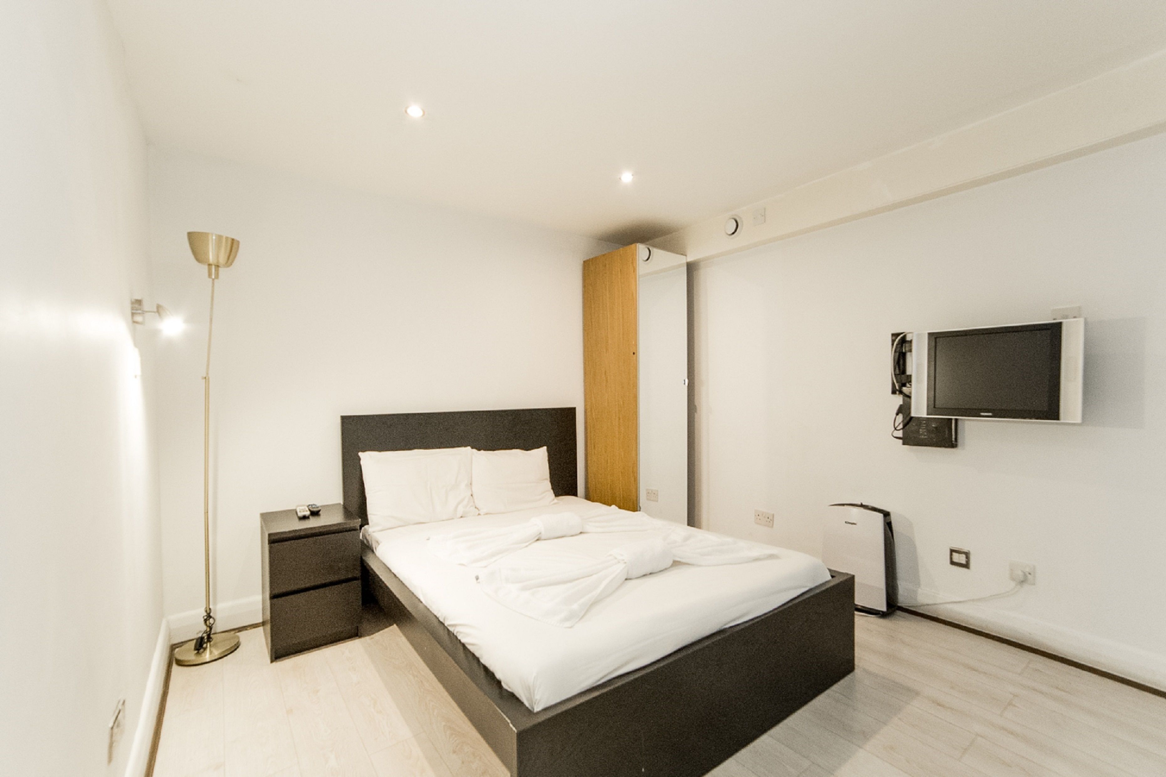 Une chambre à coucher moderne avec un lit, des tables de chevet, une lampe sur pied, un téléviseur et une armoire.