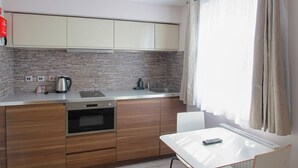 A modern kitchen with wooden cabinets, a built-in oven, a kettle, and a sink. - Imperial Court Studios (London)