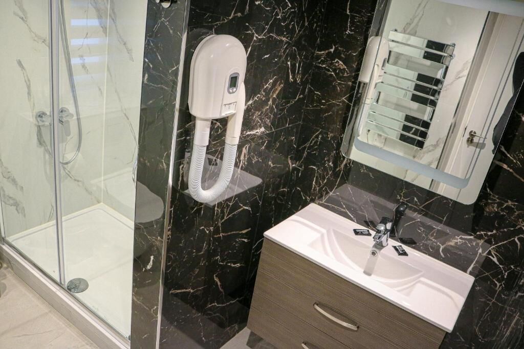 Un baño moderno con ducha de vidrio, cabezal de ducha de mano, tocador con lavamanos y espejo.