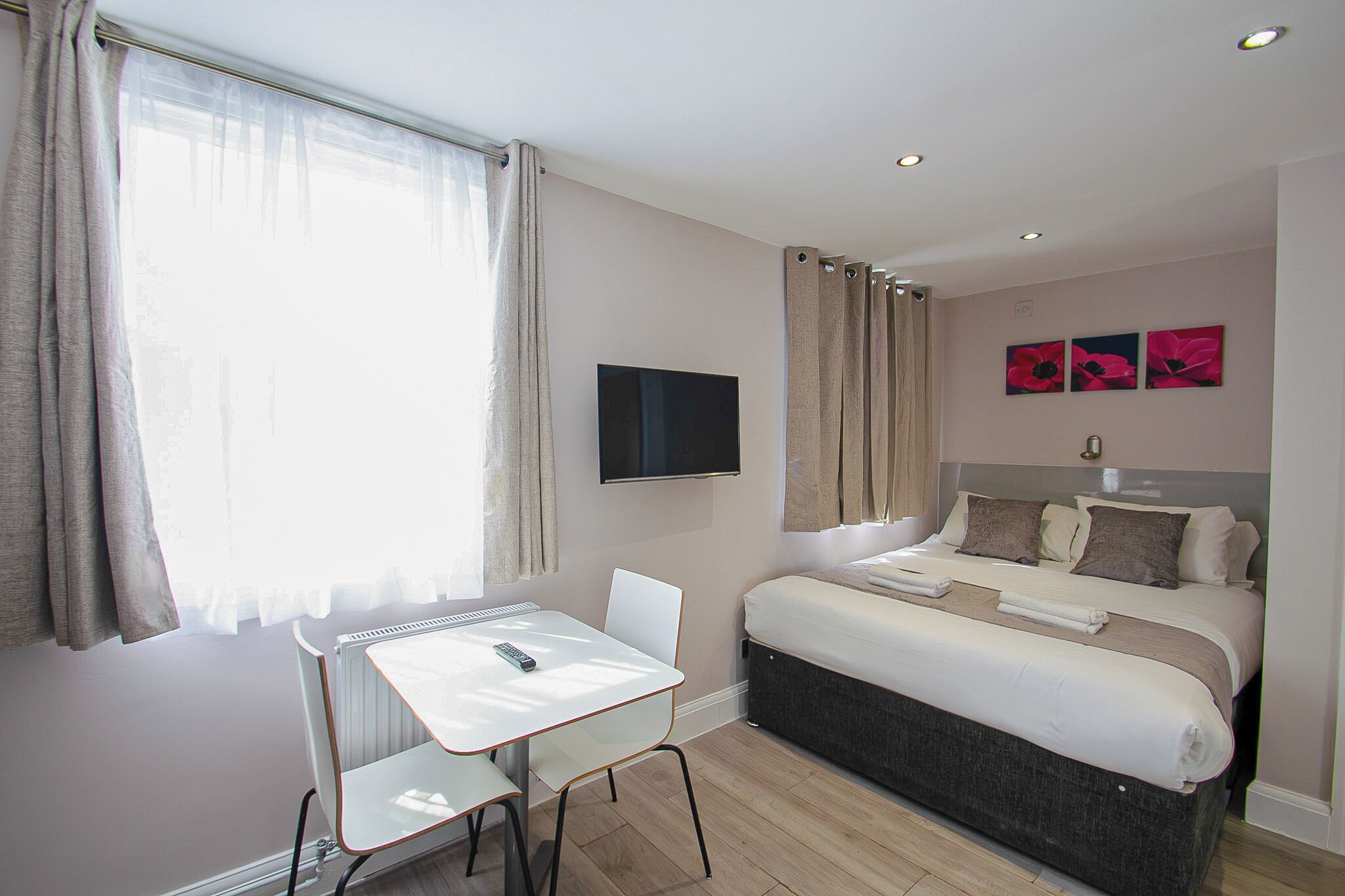 Une chambre d’hôtel avec un lit, un bureau, une chaise, une télévision et une fenêtre avec des rideaux.