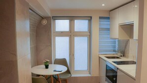 A compact kitchen with a dining area, a window with blinds, and a built-in oven. - Imperial Court Studios (London)