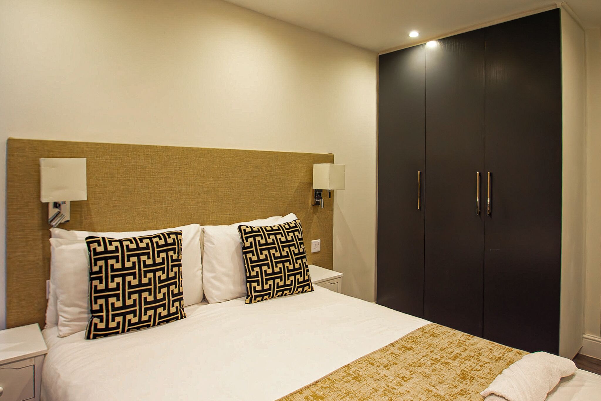 Une chambre d’hôtel avec un lit, deux oreillers, une table de chevet, une lampe et une armoire.
