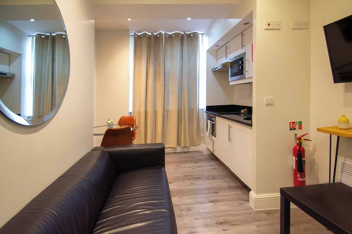 Een moderne woonkamer met een zwarte leren bank, een klein tafeltje en een aan de muur bevestigde televisie.