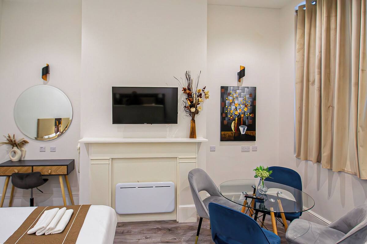 Een hotelkamer met een bed, een bureau, een stoel, een televisie, een open haard en een eethoek met stoelen en een tafel.