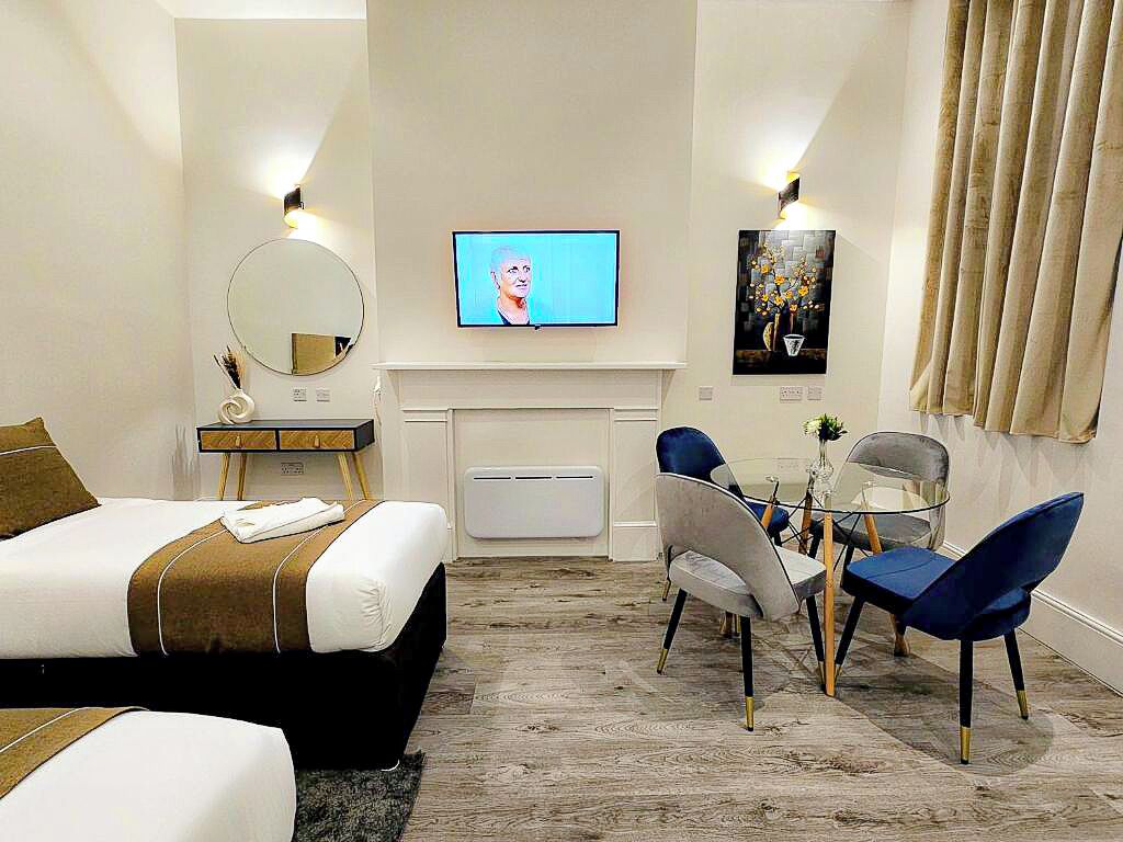 A hotel room with a bed, a desk with a chair, a television, and a fireplace.