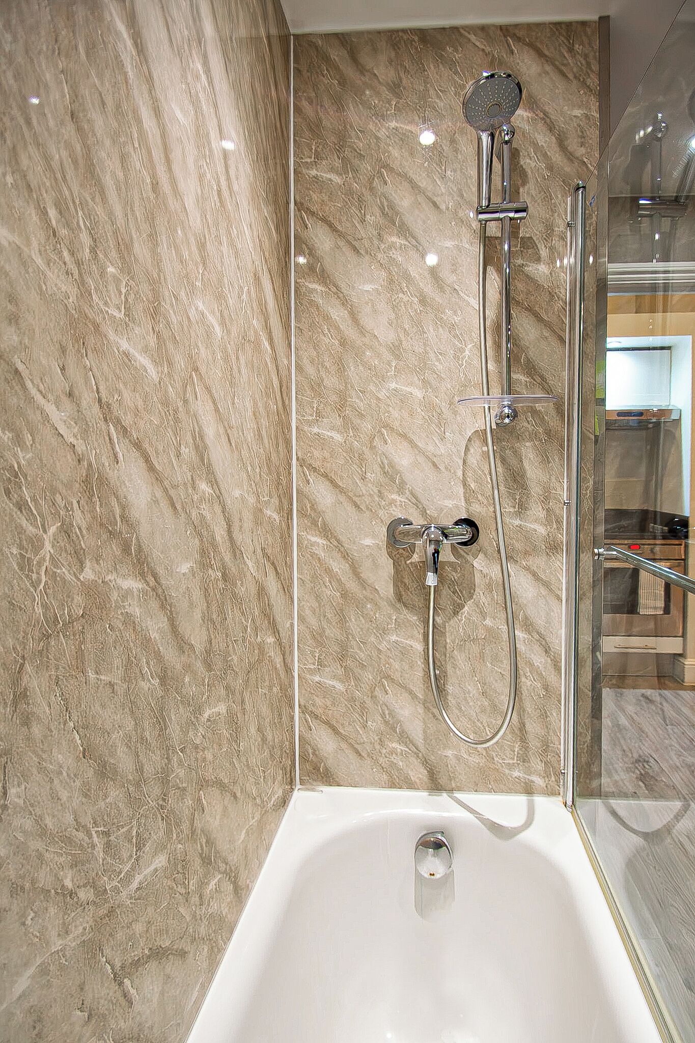 Une salle de bain moderne avec un mur en marbre, une douche à parois de verre et une baignoire blanche.