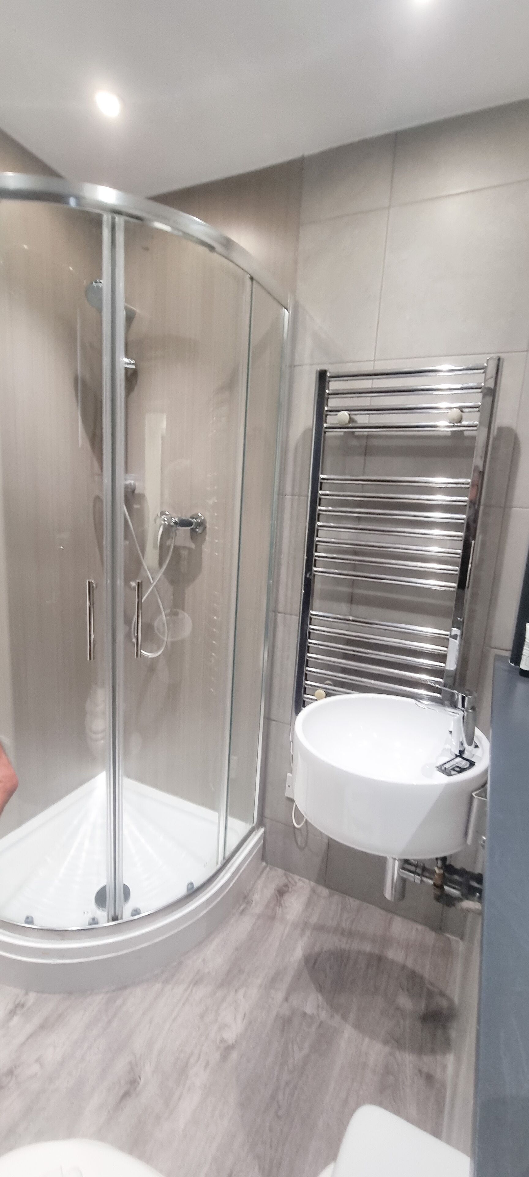 Een moderne badkamer met een douchecabine van glas, een witte wastafel en een chromen handdoekhouder.
