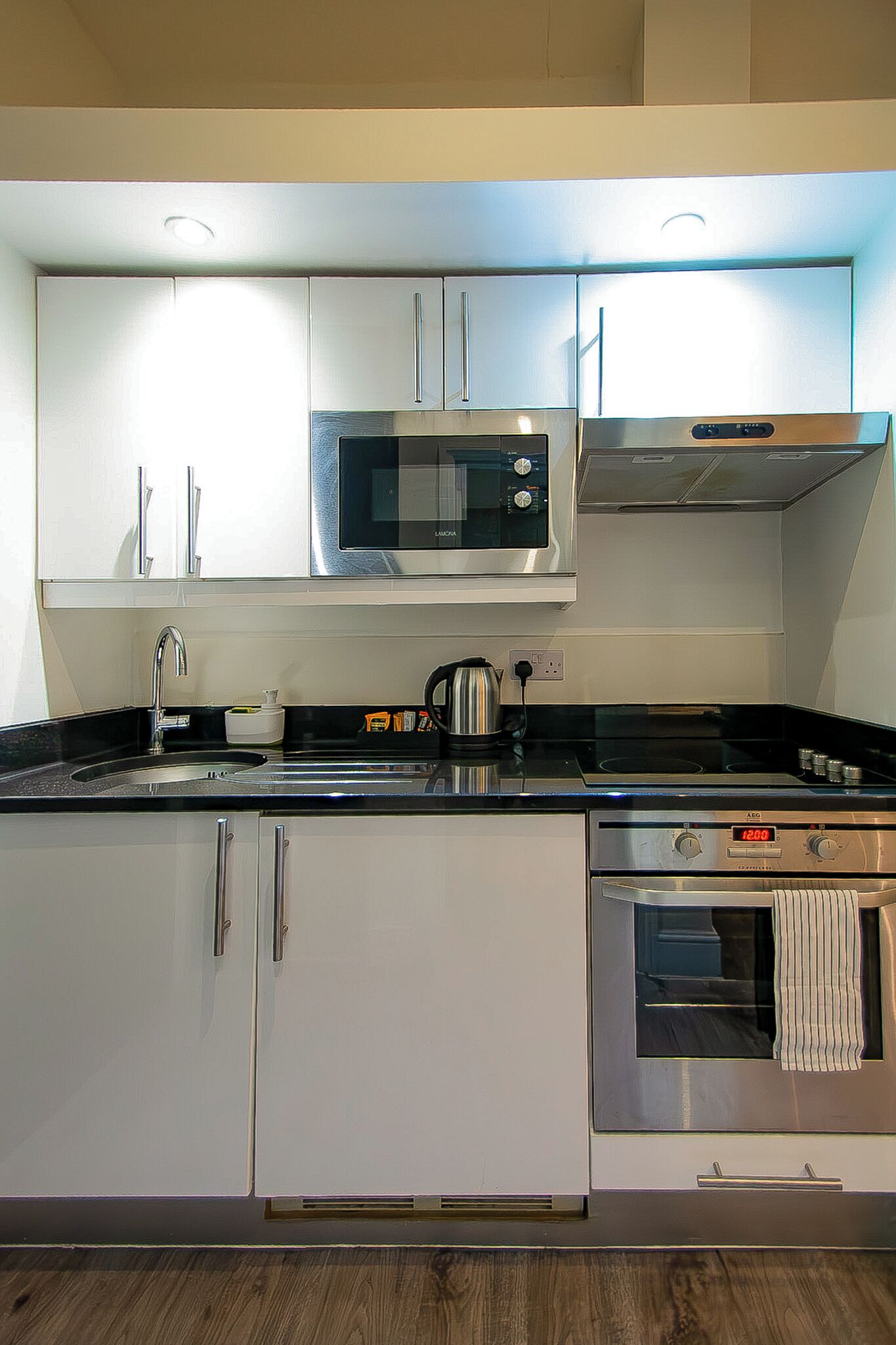 Una cocina moderna con electrodomésticos de acero inoxidable, armarios blancos y piso de madera.