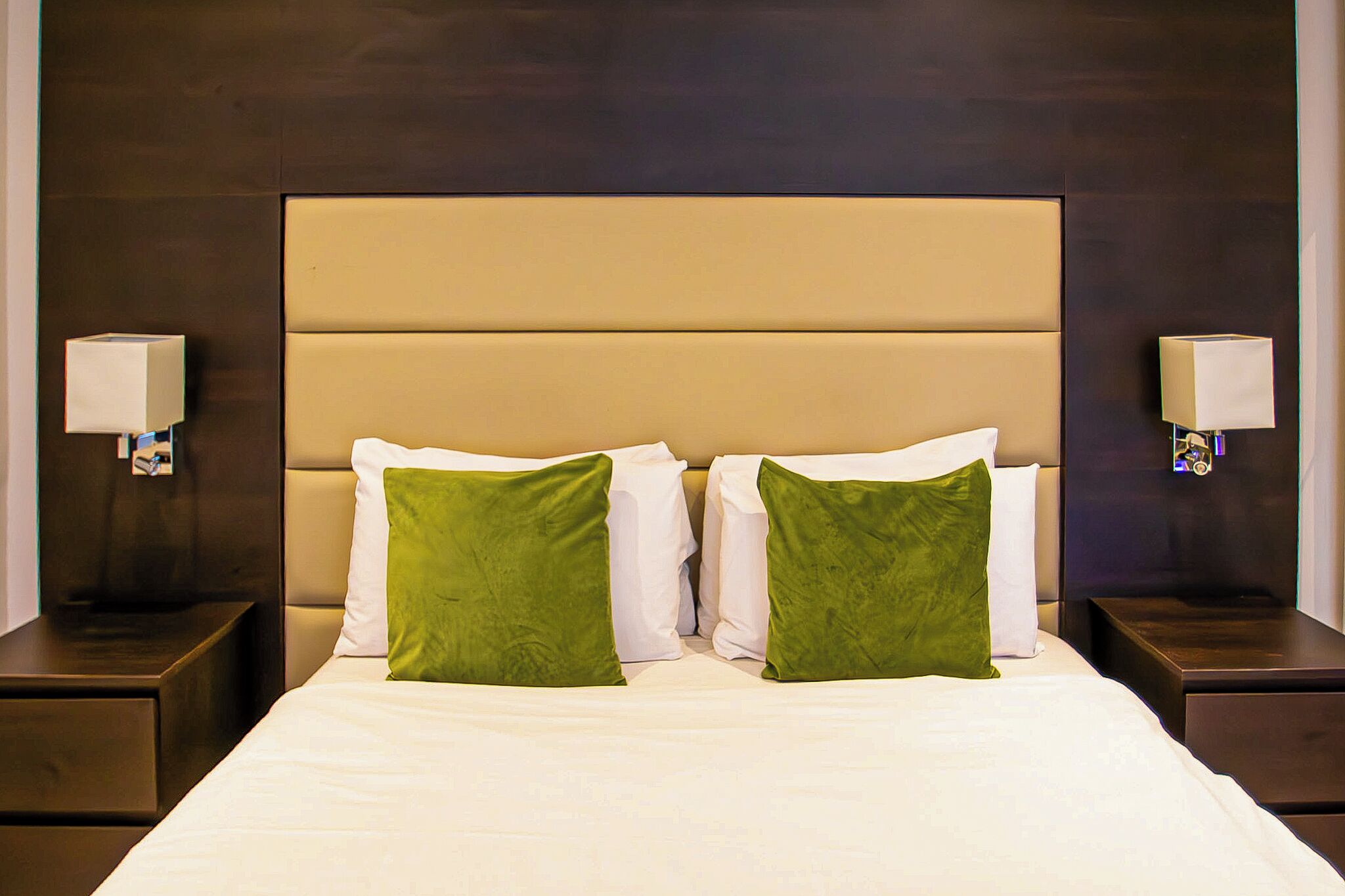 A hotel room with a large bed, two nightstands, and two wall-mounted lamps.