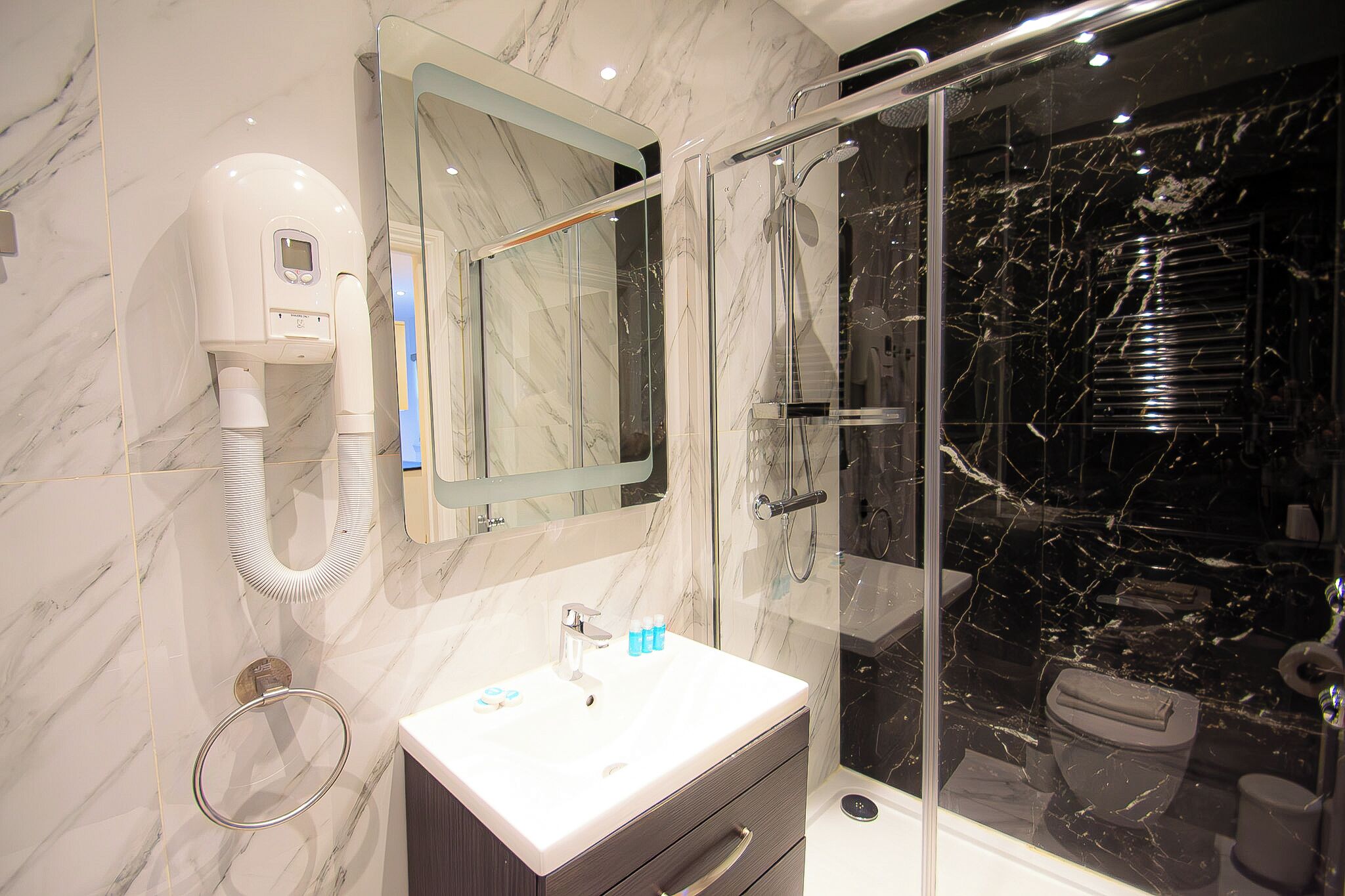 Een moderne badkamer met een marmeren wastafelmeubel, een glazen douchecabine en een ingebouwde haardroger.