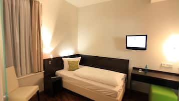 A hotel room with a bed, a desk, a chair, a TV, and a window with curtains.