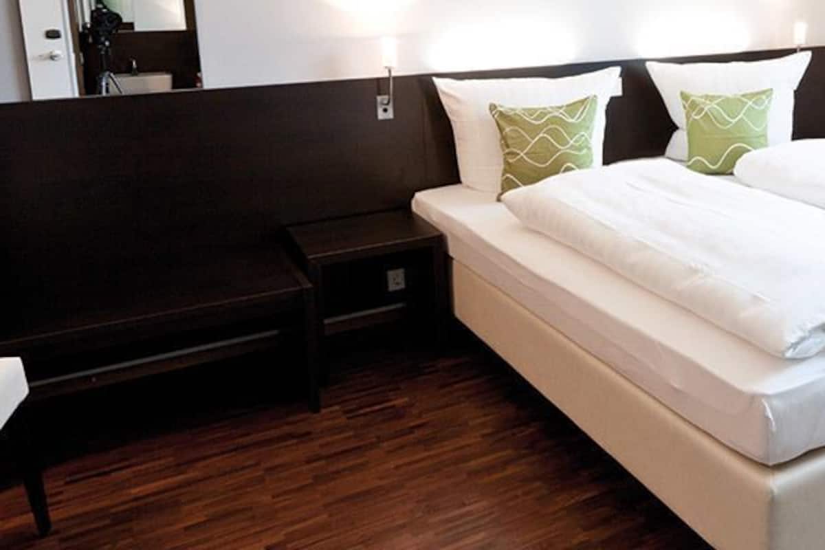 Quarto de hotel com cama, poltrona, mesa de cabeceira e espelho.