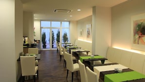 A restaurant with a long counter, multiple tables, and chairs. There are large windows at the end of the room.