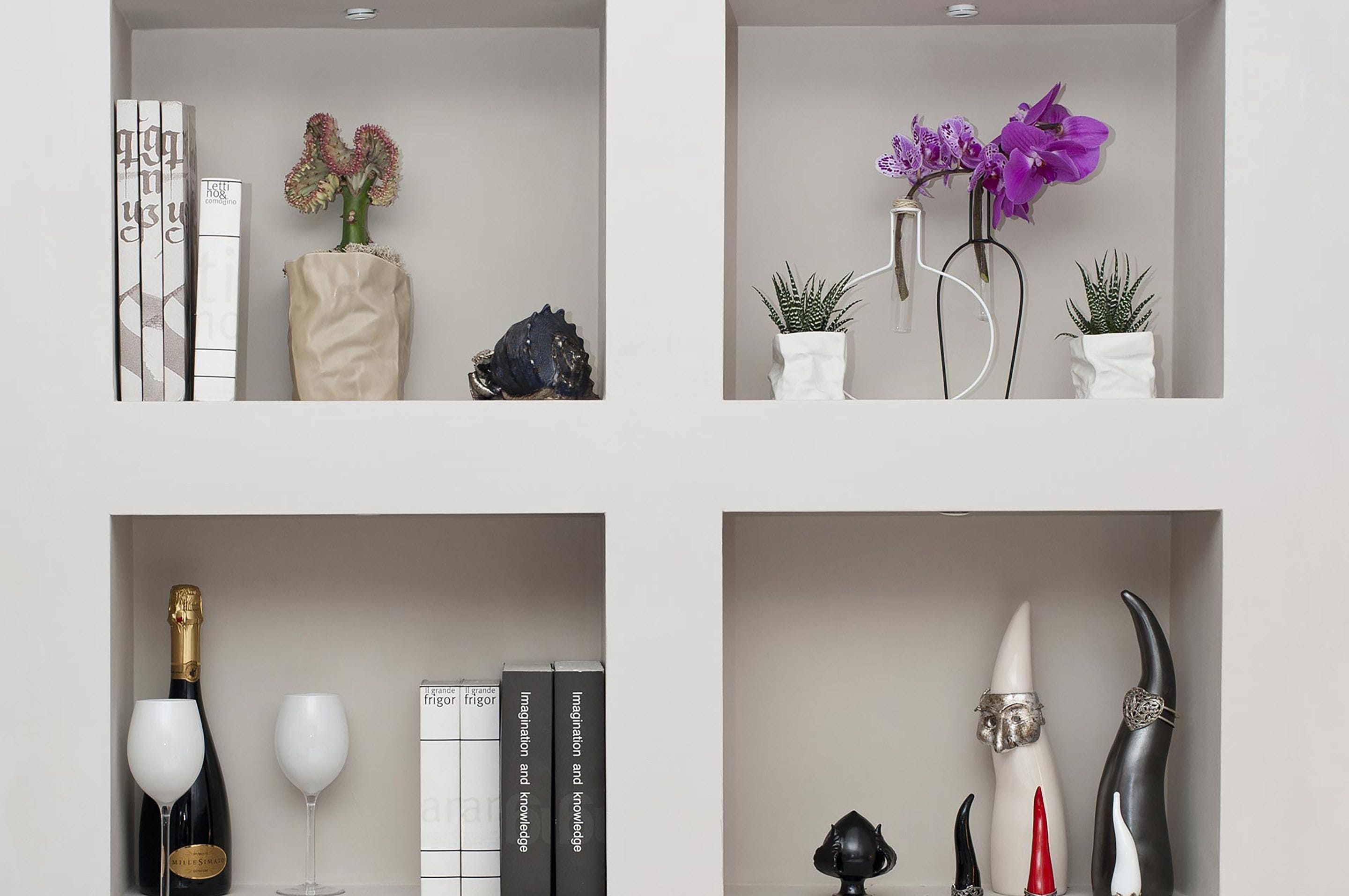 Ein modernes Interieur mit Bücherregal, Dekorvasen und einer Weinflasche.