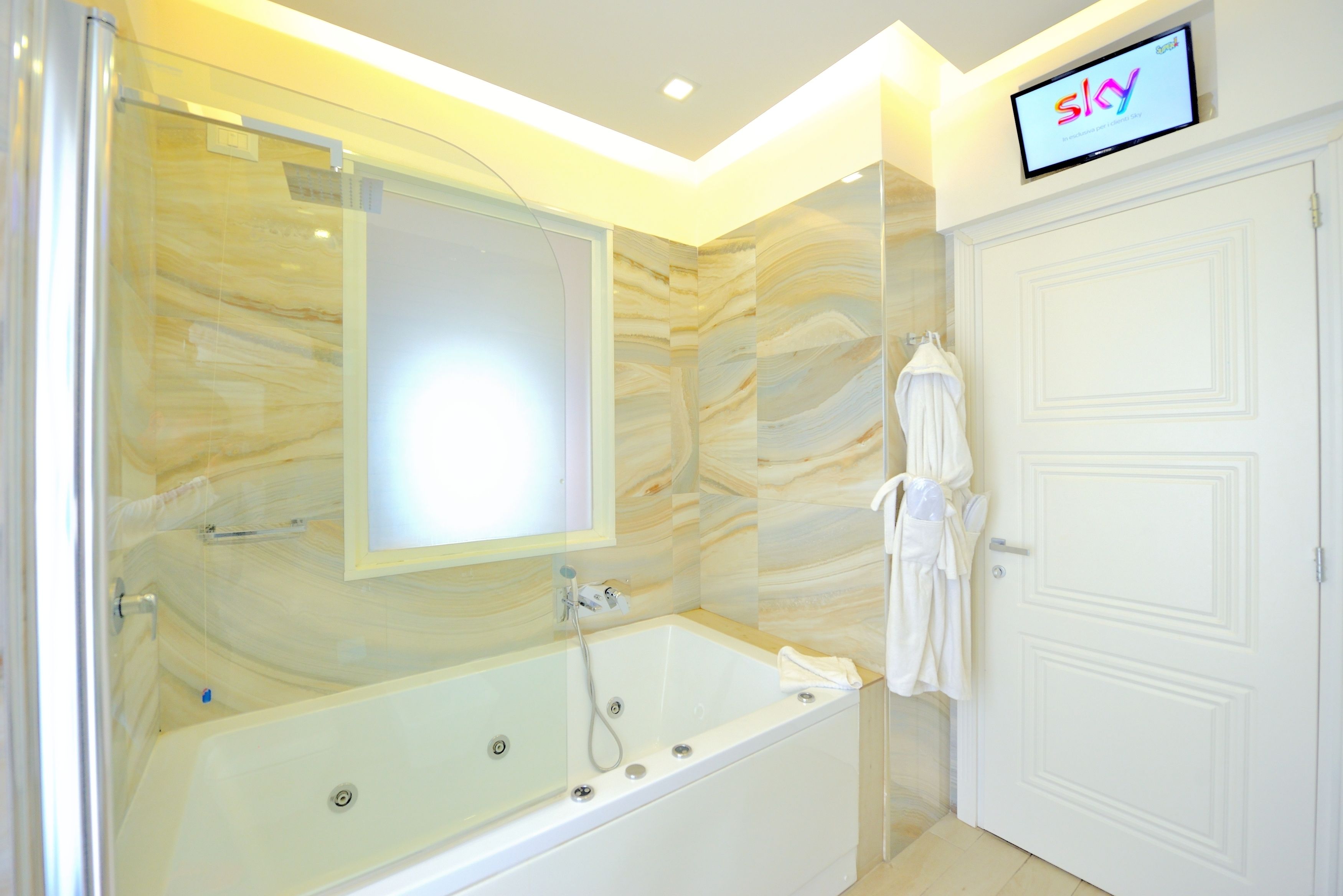 A modern bathroom with a marble wall, a glass-enclosed shower, and a white door.